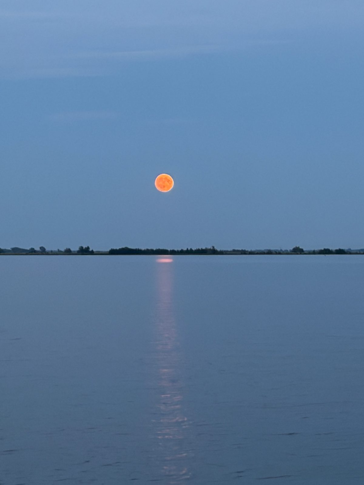 Oranje maan boven de dijk met spiegeling in het water